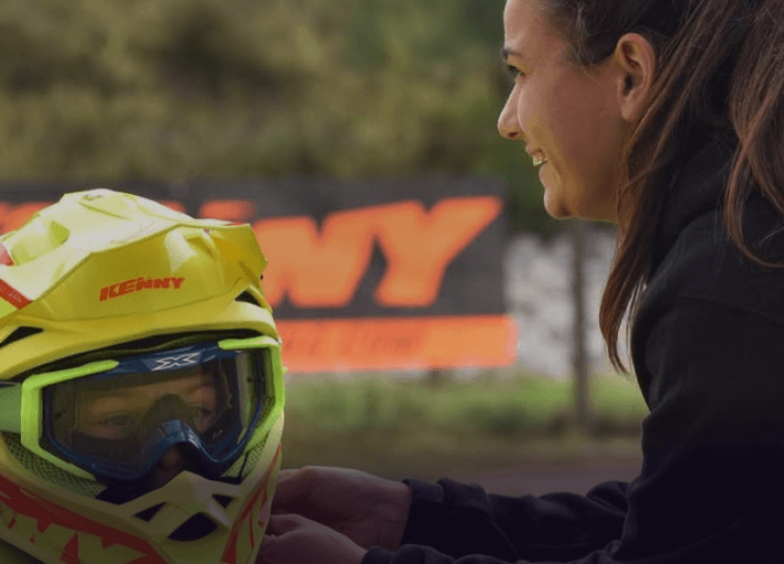 Bruna Antunes at the motocross school helping a student put on a helmet