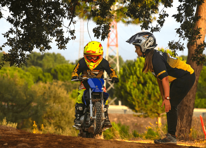 Bruna Antunes teaching young children how to ride a motorcycle at a motocross school.